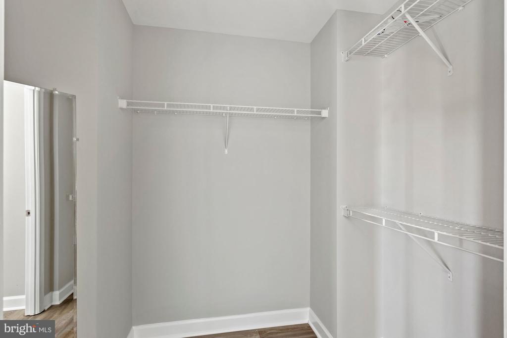 Walk-in closet with white wire shelving on three walls and wood flooring.
