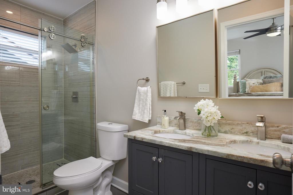 Bathroom with a glass-enclosed gray-tile shower and dark vanity with stone countertop.