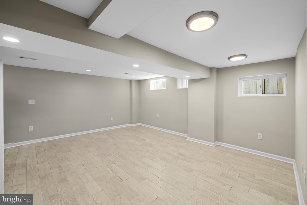 Finished basement room with light tile flooring, gray walls, and small high windows.