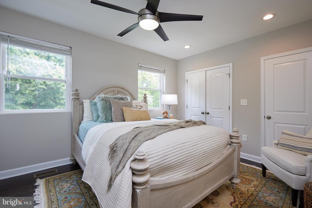 Staged bedroom with a large white bed, patterned rug, two windows, and ceiling fan.