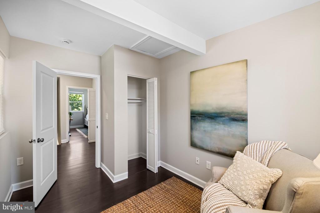 Sitting area with a cream sofa, abstract wall art, dark hardwood floors, and an open closet.