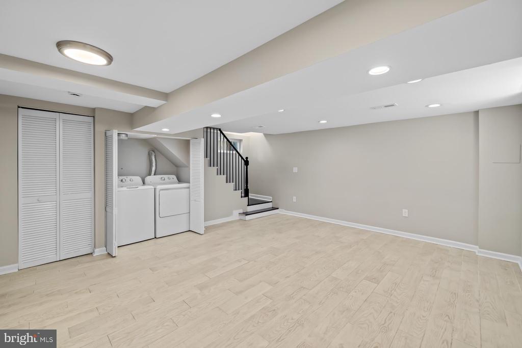 Finished basement with light wood flooring, laundry closet, and staircase.