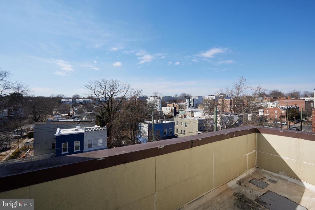 Apartment balcony overlooking low-rise neighborhood homes and leafless trees under a clear blue sky.
