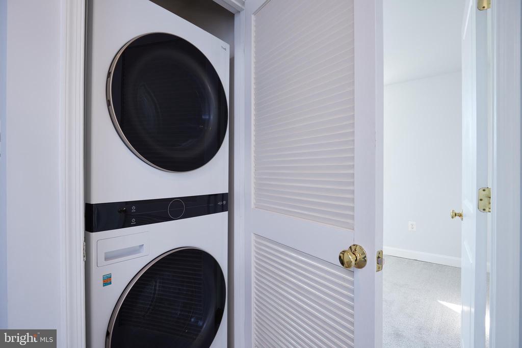 Stacked washer and dryer in a laundry closet with open louvered doors.