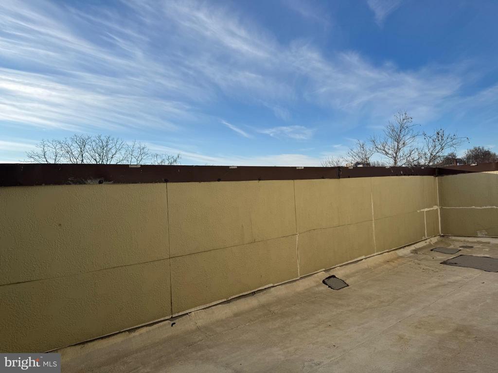 Empty rooftop terrace with tan privacy walls and a wide paved surface.