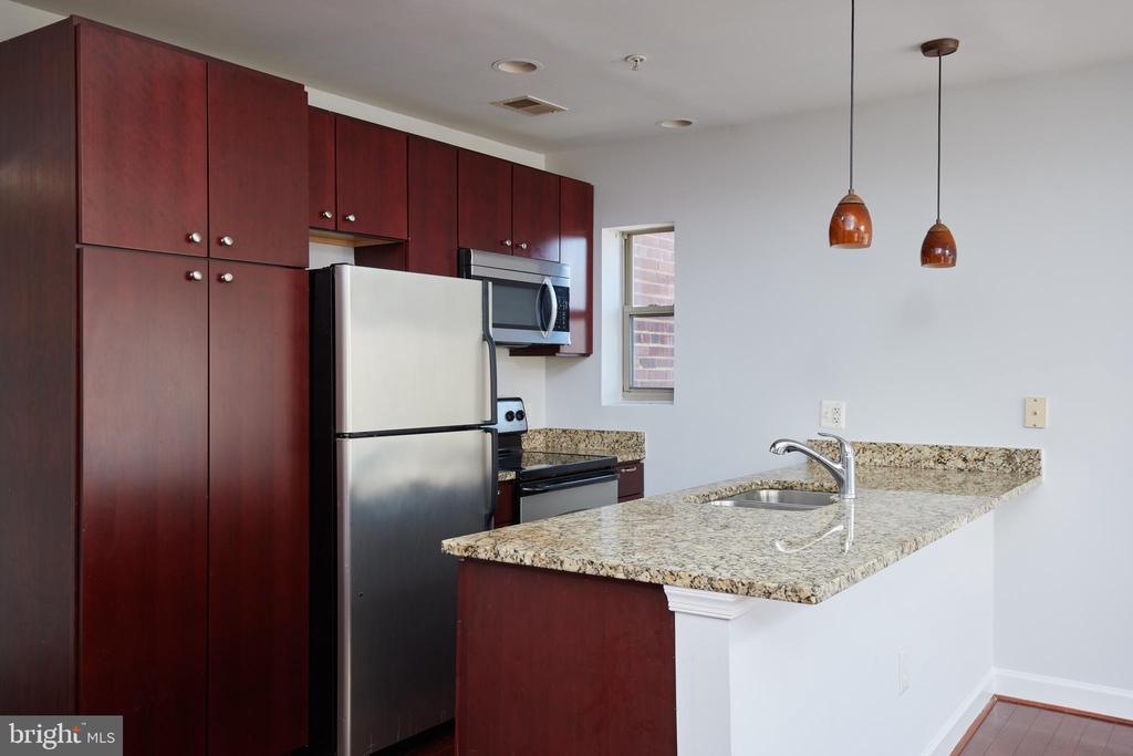 Kitchen with dark wood cabinets, stainless appliances, and a granite breakfast bar with sink.