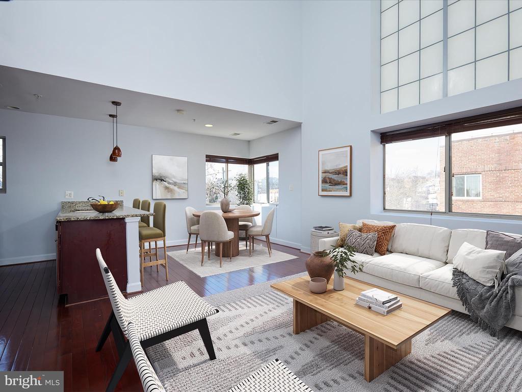 Staged open-plan living room with a white sofa, wood coffee table, dining area, and kitchen peninsula.