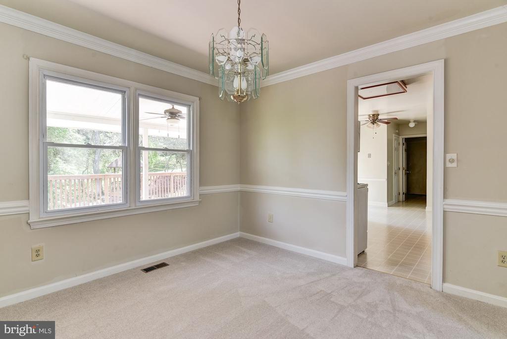 Empty dining room with chandelier, two deck-facing windows, and an open doorway to a tiled area.