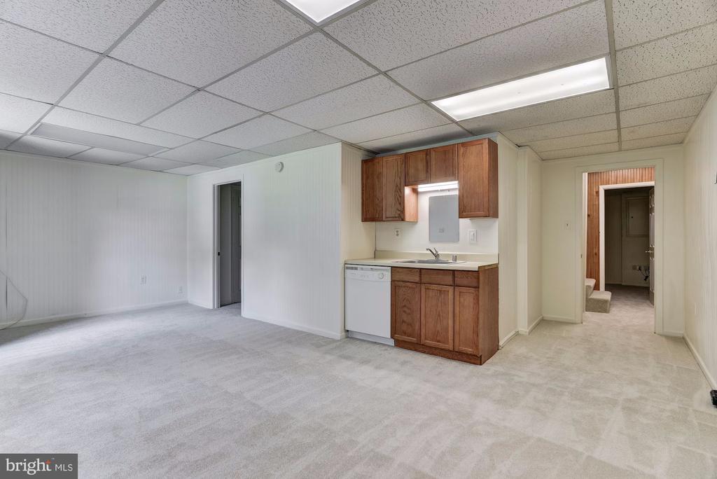 Finished basement room with a compact wood-cabinet kitchenette and hallway to a bathroom.