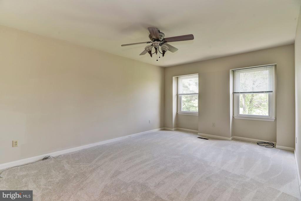 Empty carpeted bedroom with a ceiling fan and two windows with blinds.