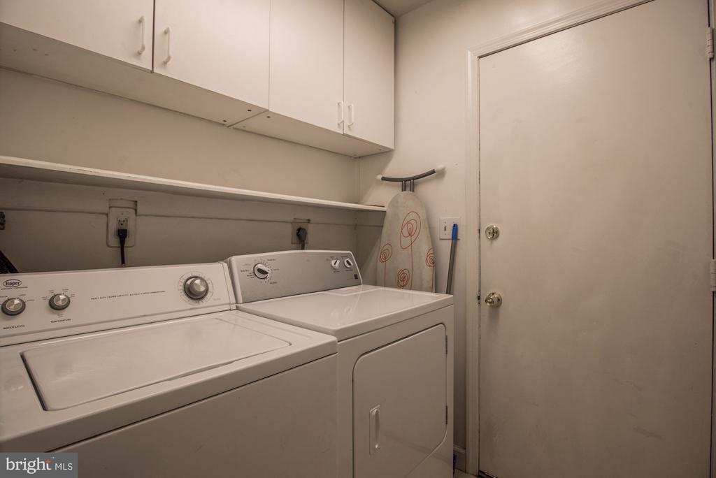 Laundry room with a top-loading washer and dryer beneath white storage cabinets.