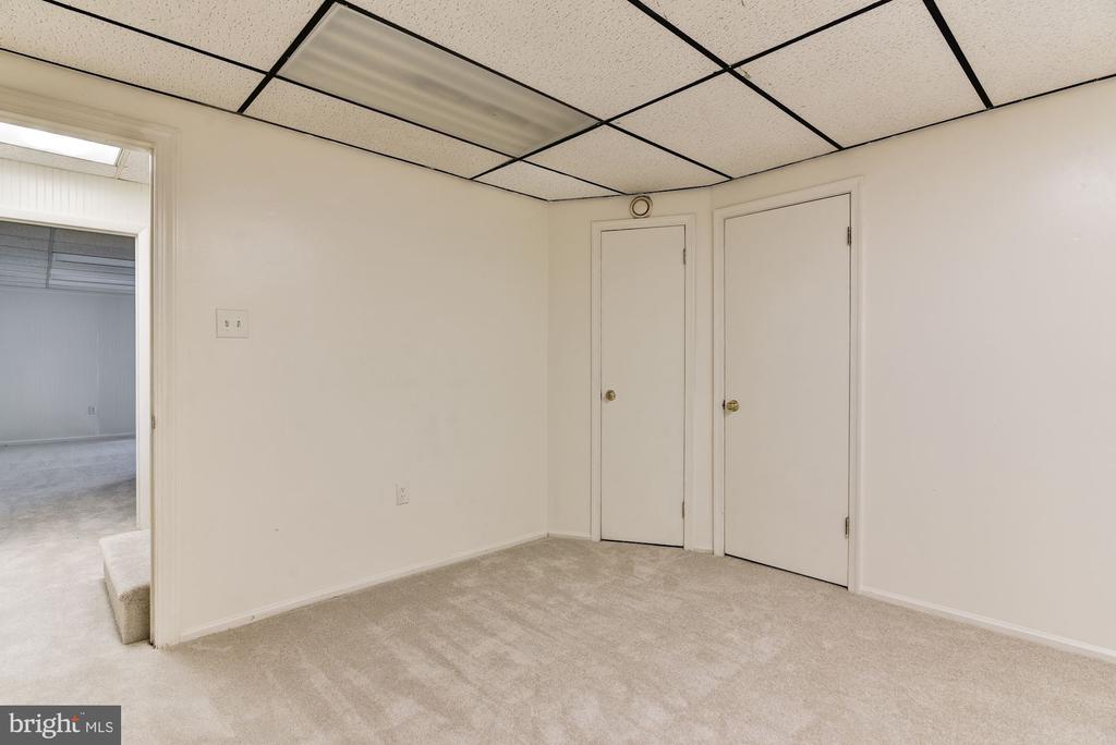 Empty carpeted room with a suspended ceiling and two closed doors.