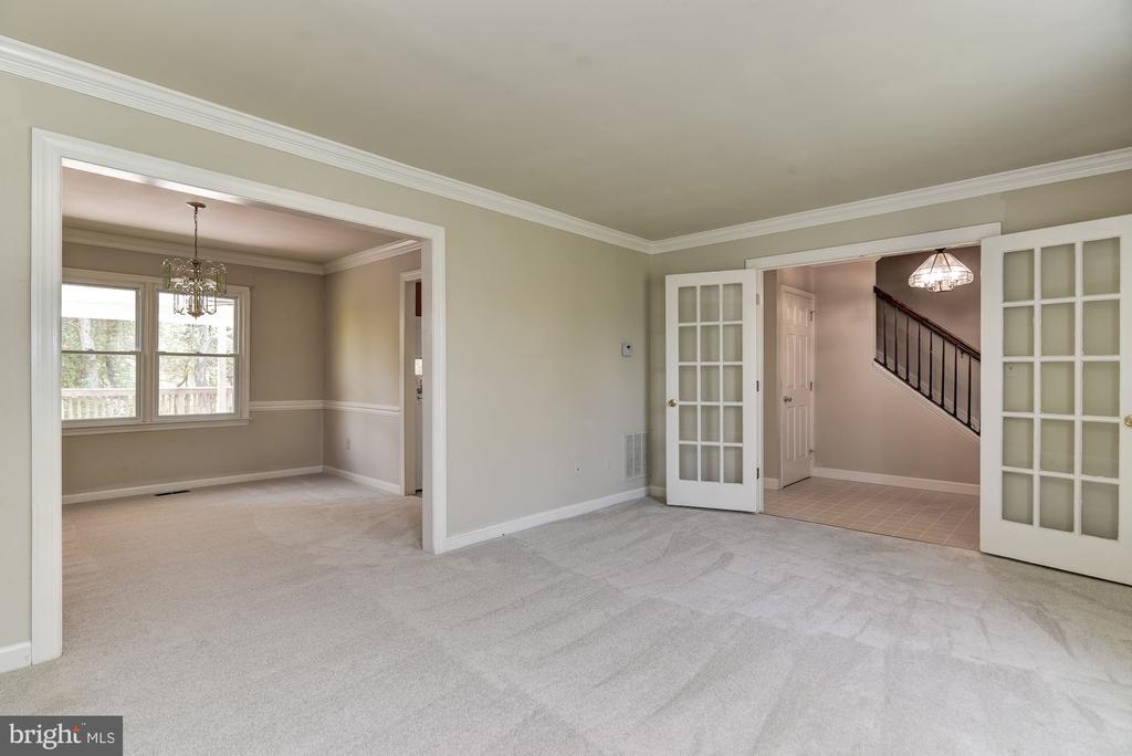 Empty carpeted living room opening to a dining room and tiled foyer with a staircase.
