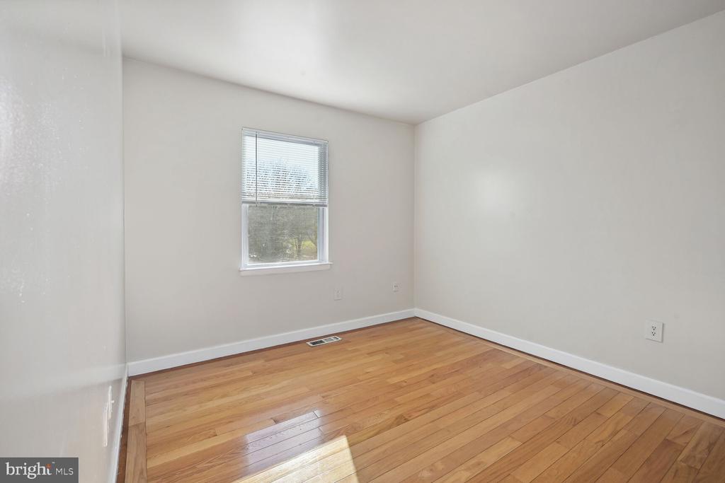 Empty room with polished hardwood floors and a window with blinds.