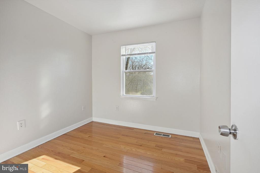 Empty bedroom with hardwood floors, neutral walls, and a window with blinds.
