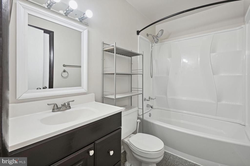 Bathroom with a white vanity, dark cabinets, and a tub-shower surround.