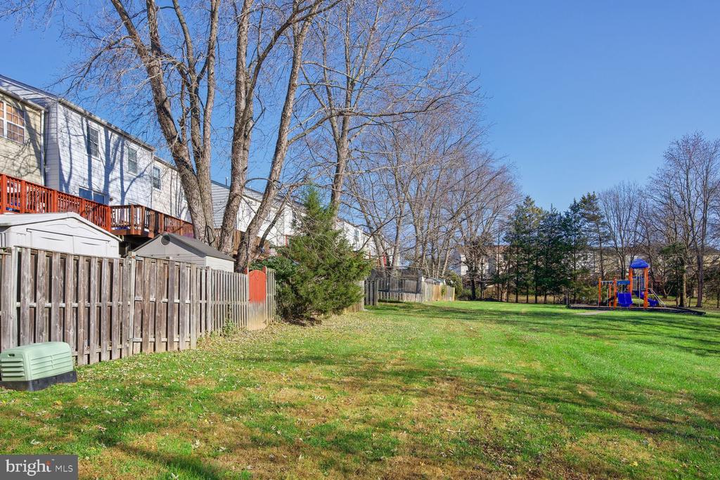 Grassy open space behind townhouses, with fenced yards and a colorful playground in the distance.