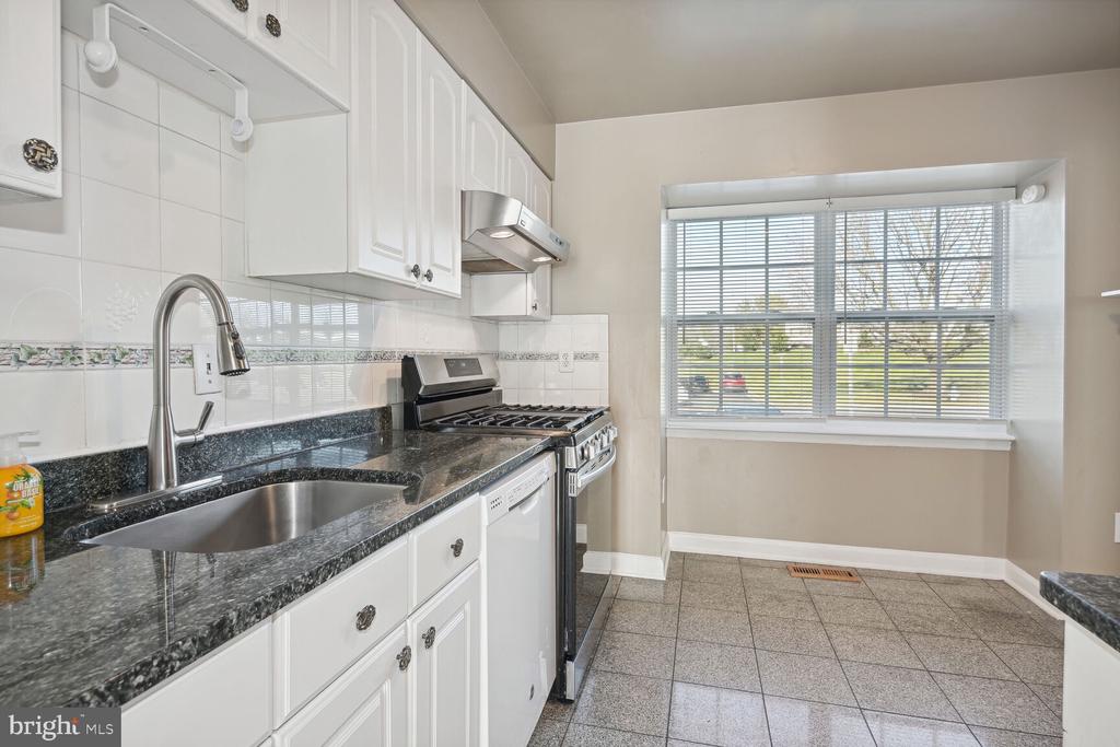 Kitchen with white cabinets, dark granite counters, stainless gas range, and a large window with blinds.