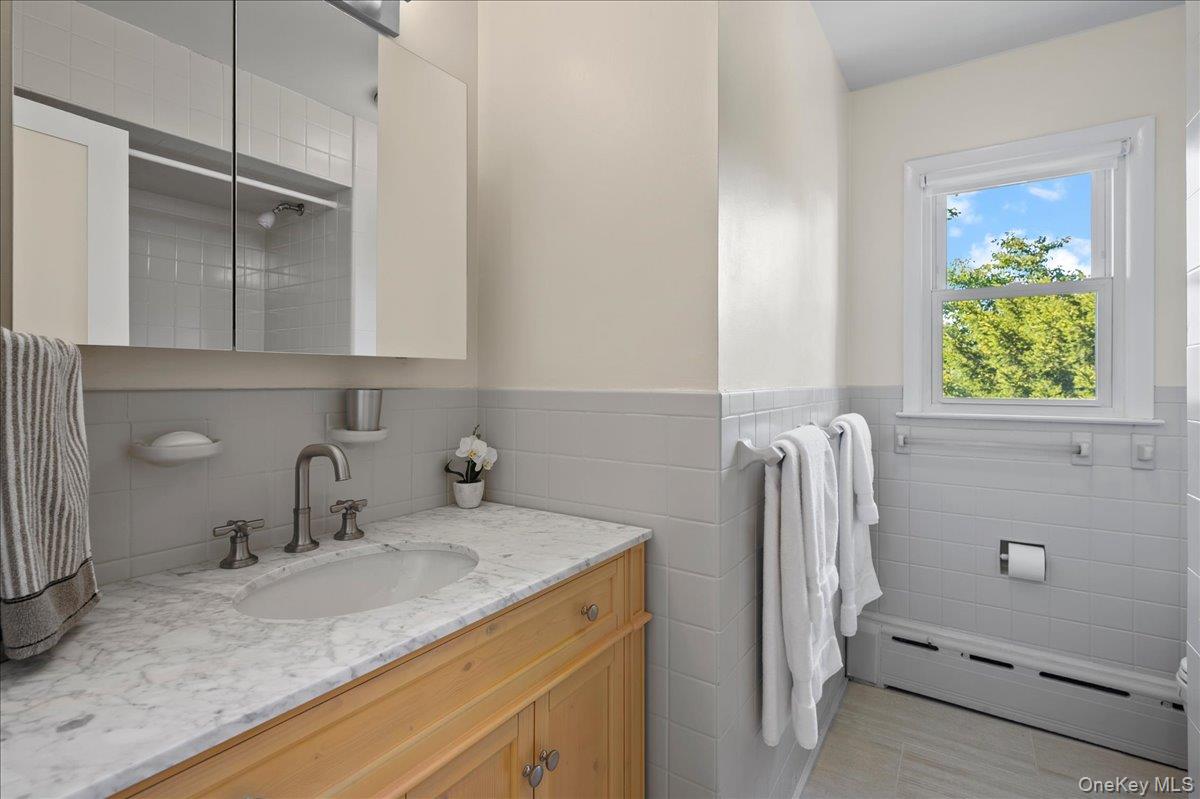 Bathroom with a marble vanity, mirrored cabinets, and a white tub beneath a window.
