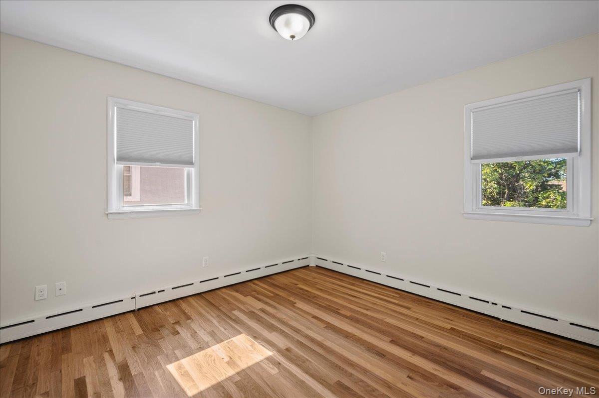 Empty room with hardwood floors, two windows, and baseboard heating.