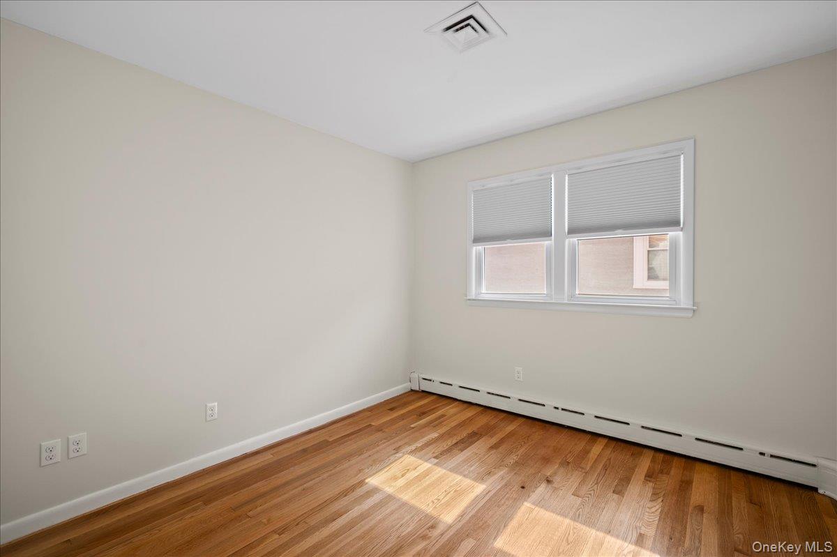 Empty bedroom with a double window, baseboard heater, and sunlit hardwood floors.