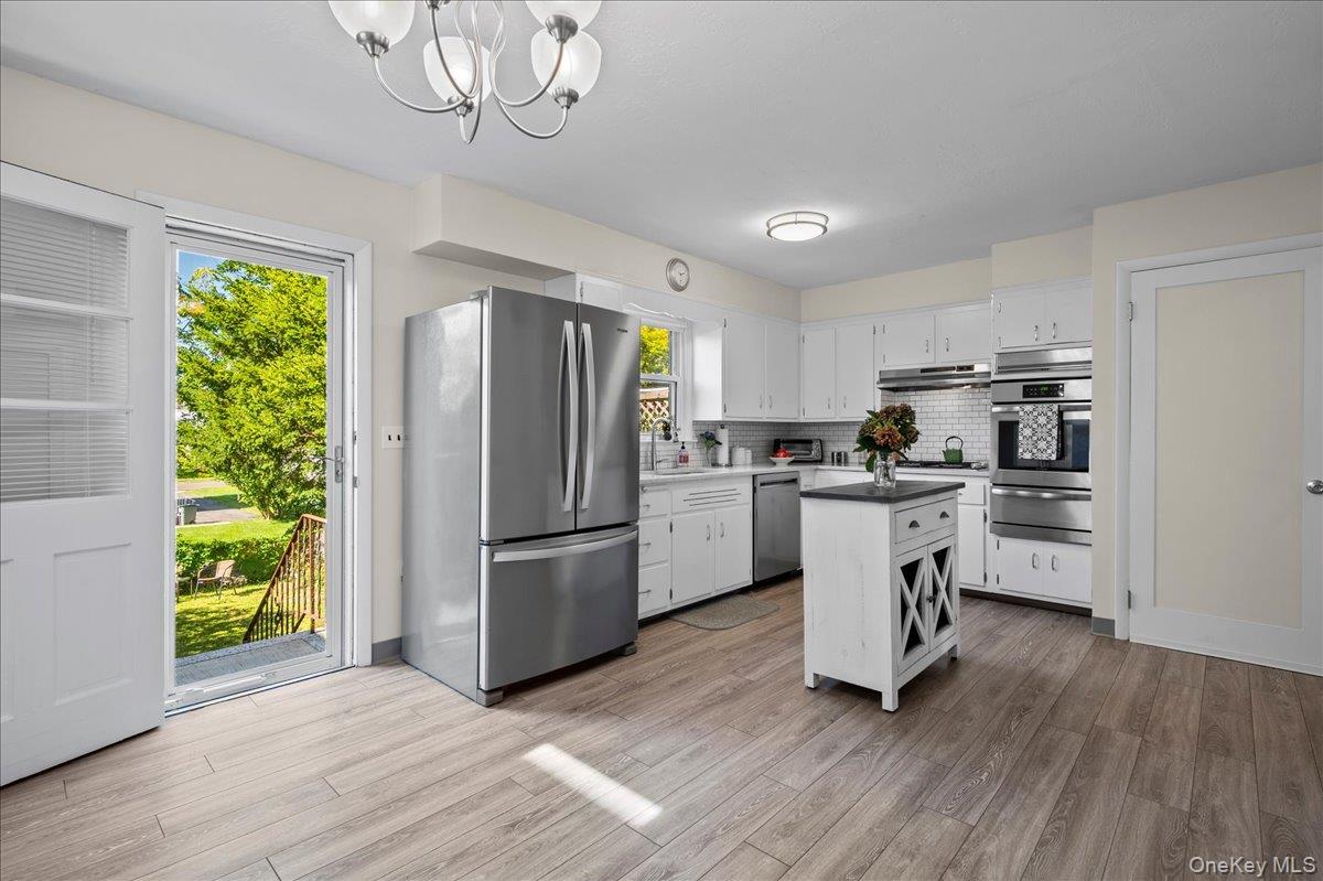 Kitchen with white cabinets and stainless steel appliances, opening to a green yard through a glass door.
