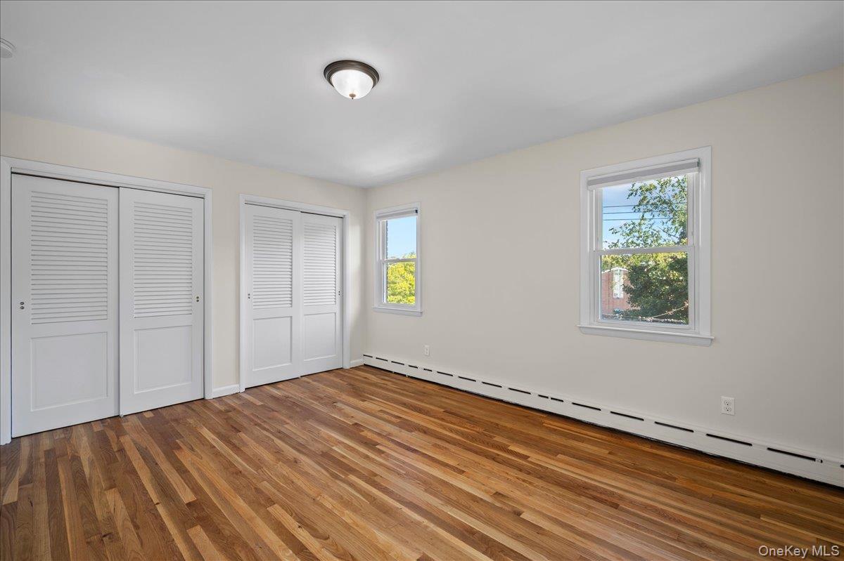 Empty bedroom with hardwood floors, louvered closet doors, and two windows.