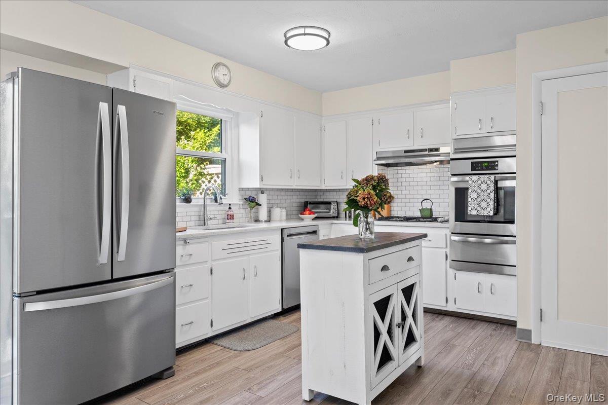 White kitchen with stainless steel appliances, subway-tile backsplash, and a dark-topped central island.