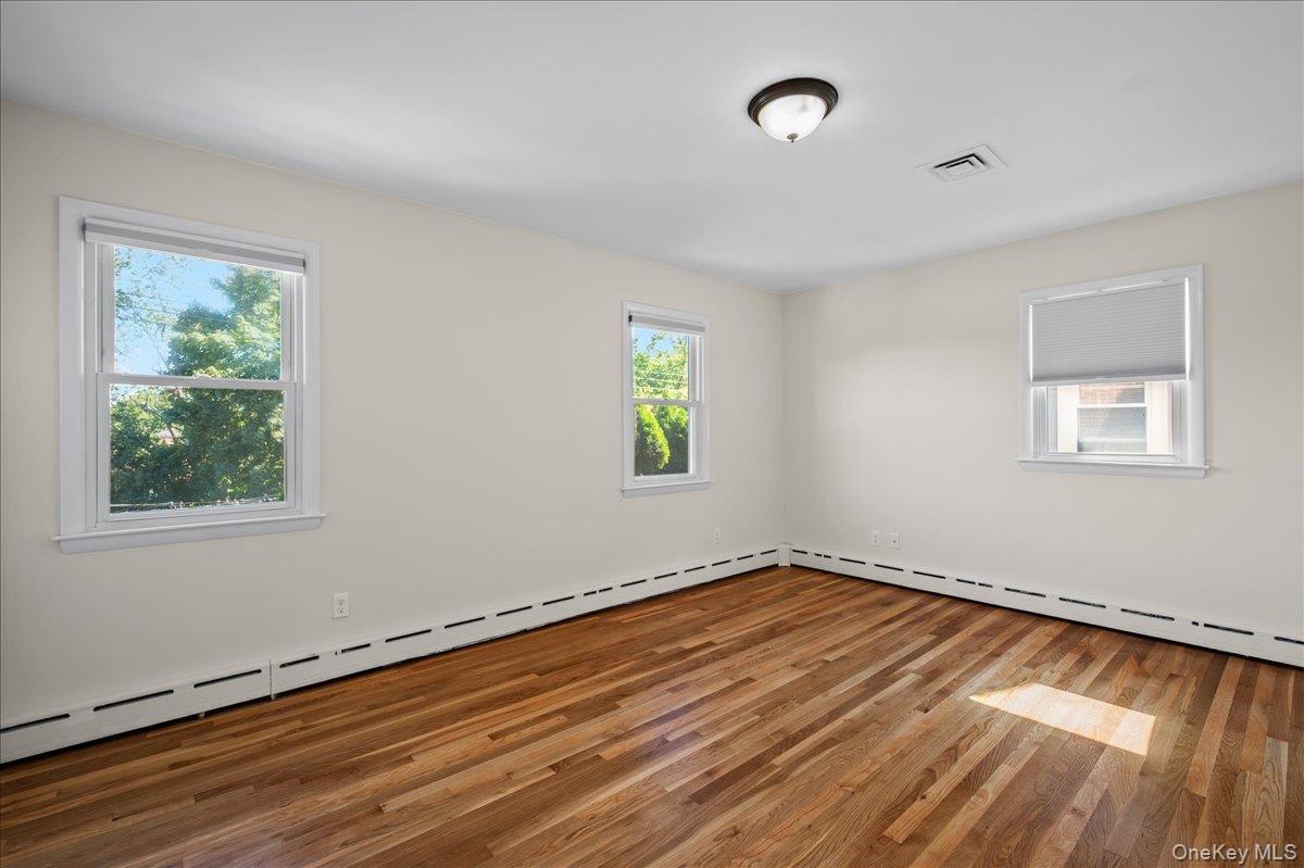 Empty room with polished hardwood floors, three windows, and baseboard heating.