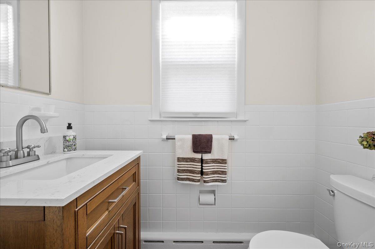Bathroom with a wood vanity, white tile, shaded window, and towel rack.