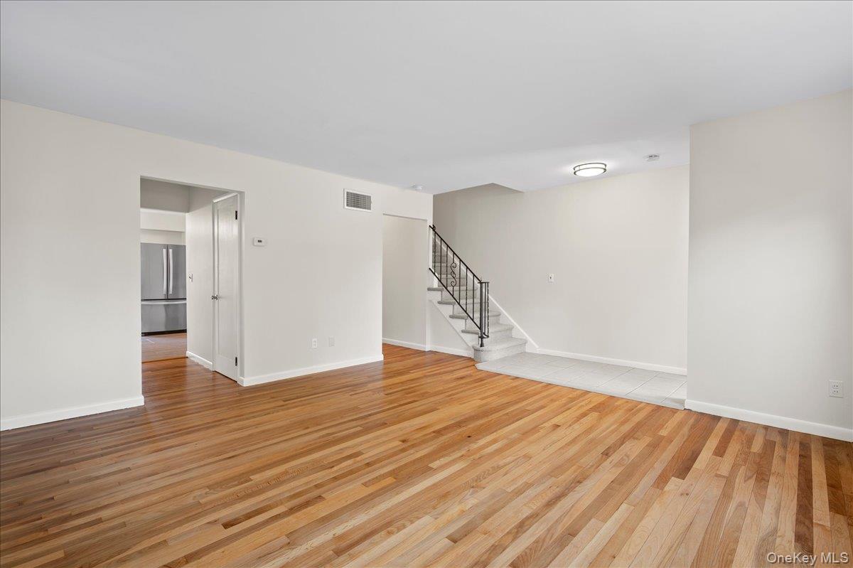 Vacant living room with polished hardwood floors and a staircase with dark metal railing.