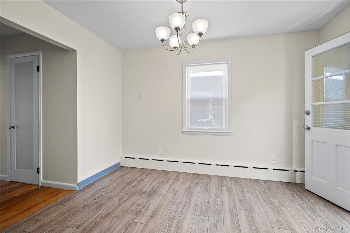 Empty room with light plank flooring, a chandelier, and a long white baseboard heater.