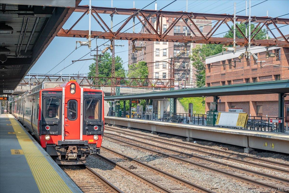 Red commuter train at Harrison station, with overhead wires and brick buildings behind the platforms.