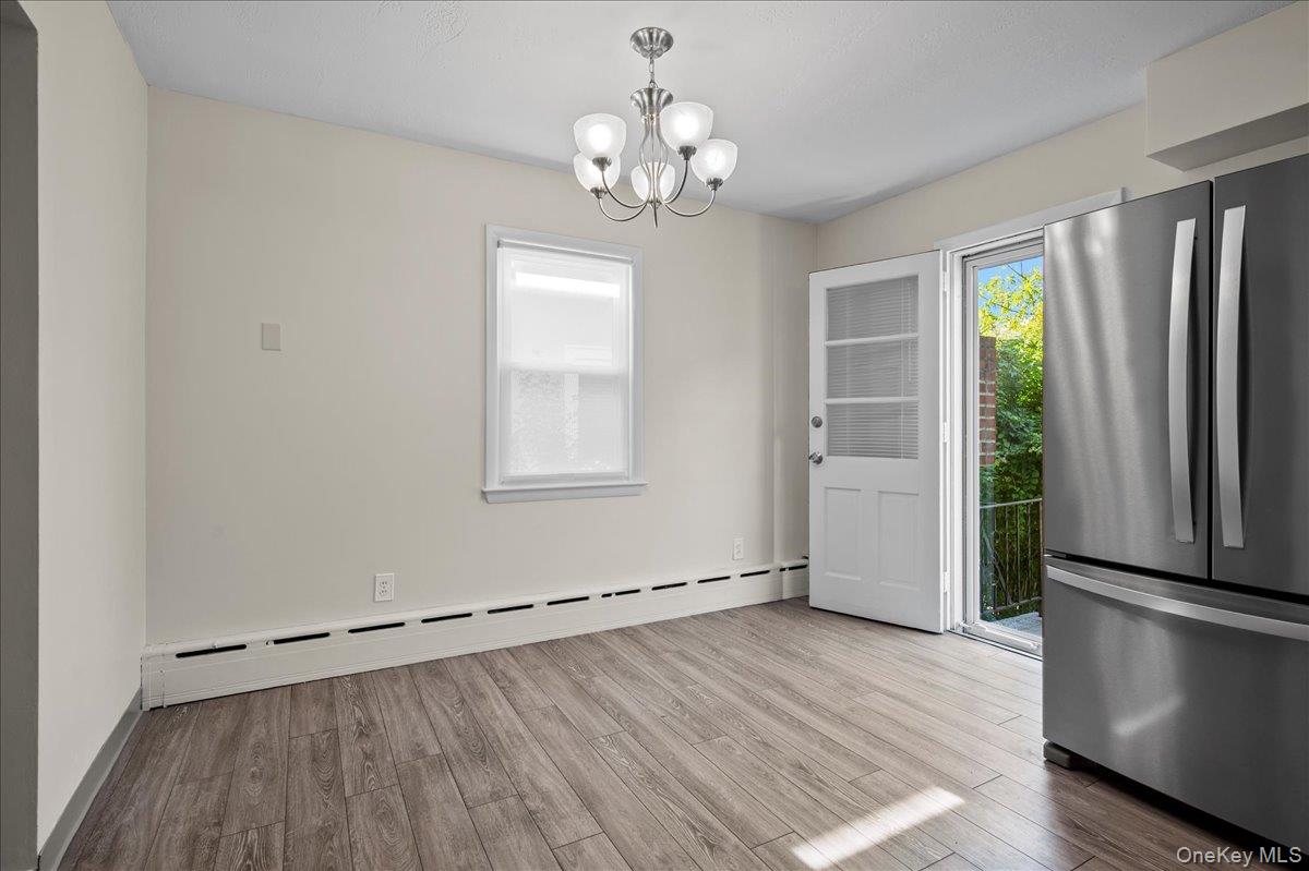 Vacant kitchen with gray plank flooring, stainless steel refrigerator, and an open door to greenery.