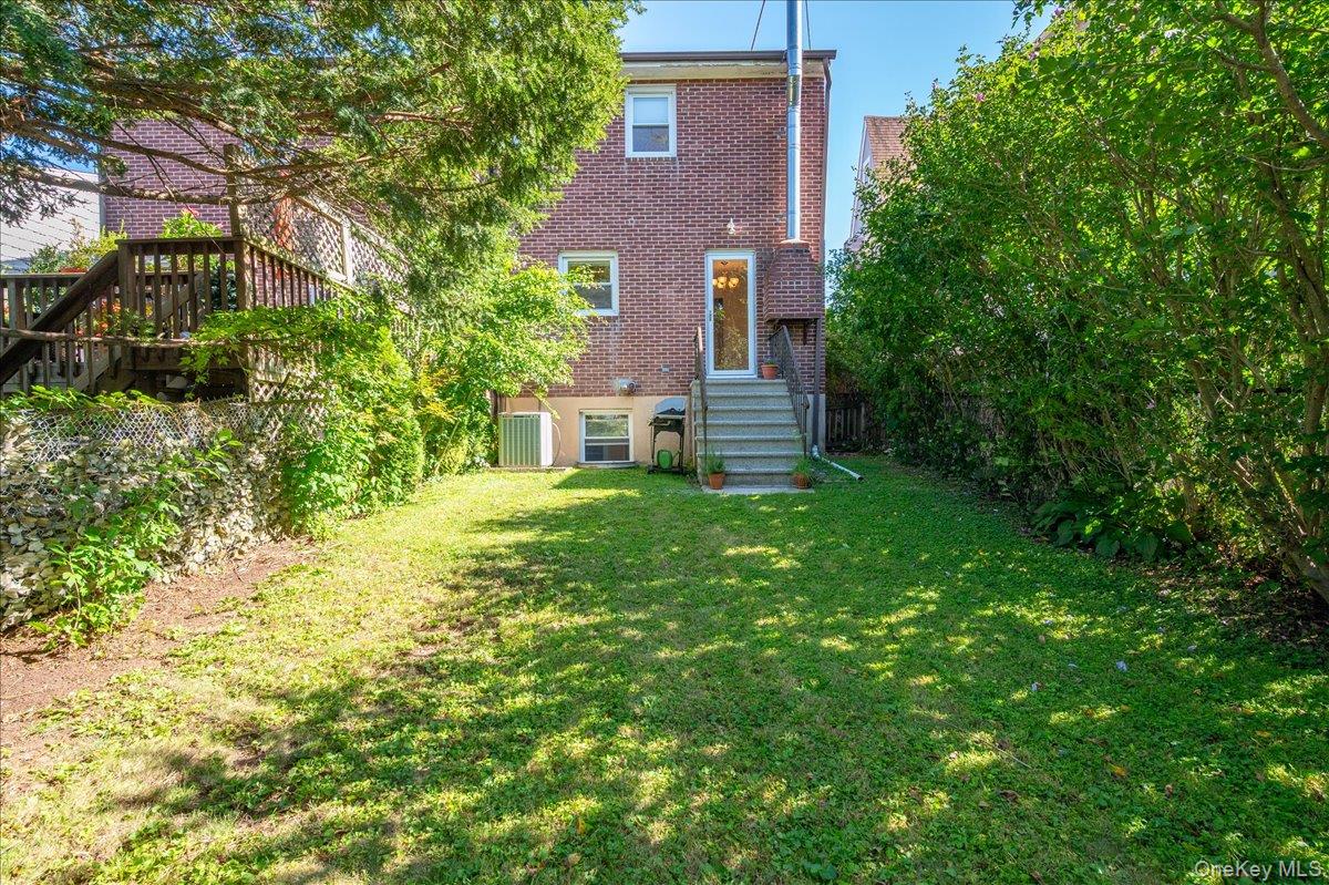 Brick residence with rear steps, a raised deck, and a grassy yard shaded by mature trees.