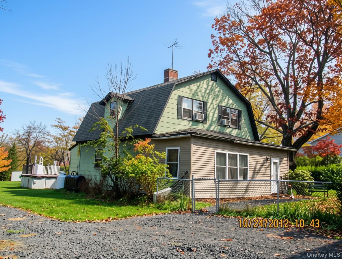 Green and beige two-story home with a fenced yard and autumn trees.