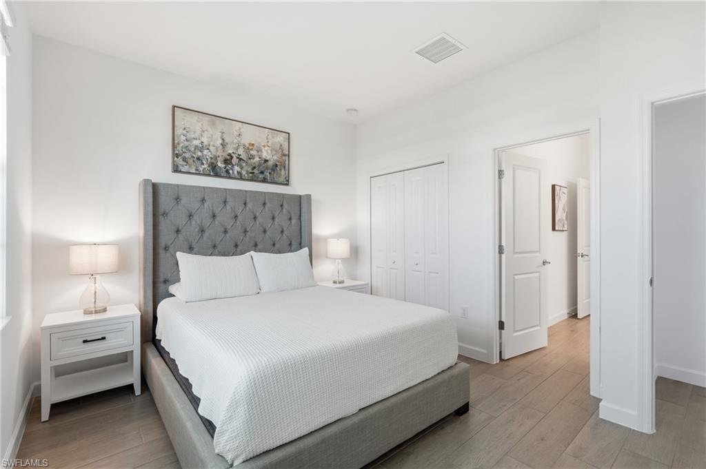 Bedroom with a gray tufted bed, white bedding, matching nightstands, and light wood-look flooring.