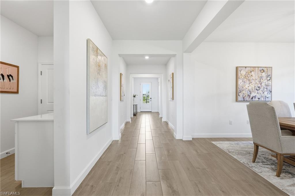 Bright hallway with wood-look tile flooring, artwork, and a view toward the glass-paneled front door.