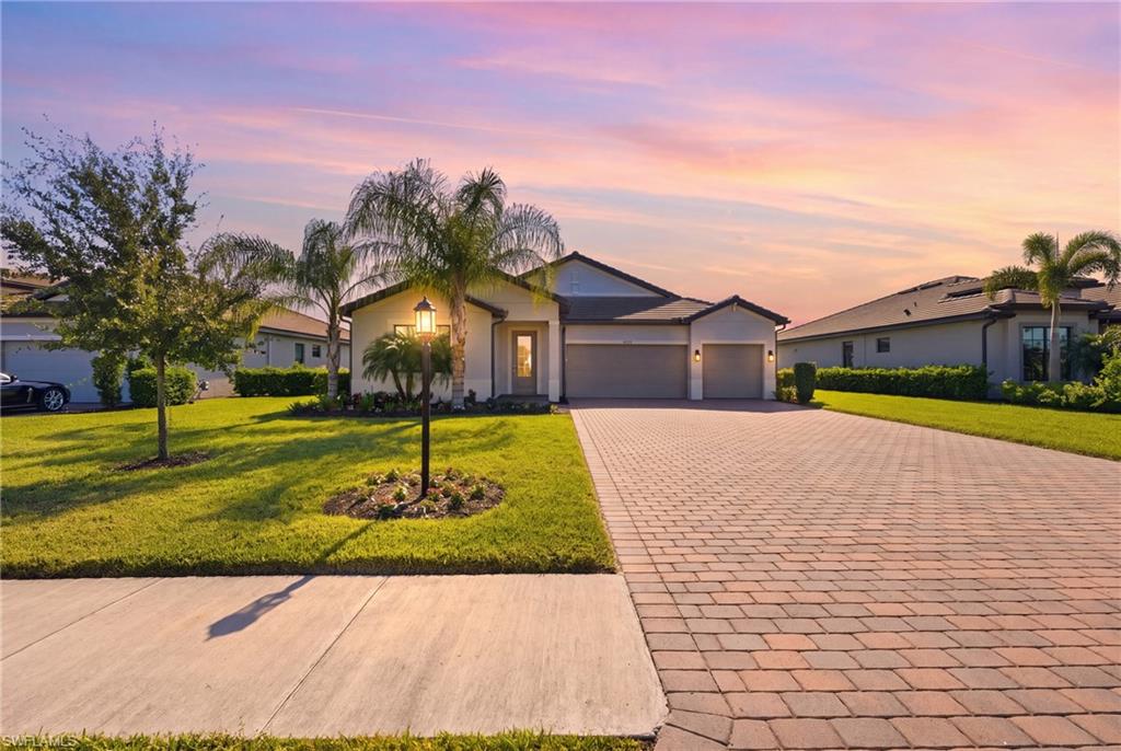 Single-story Florida home with a broad paver driveway and palm trees at sunset.