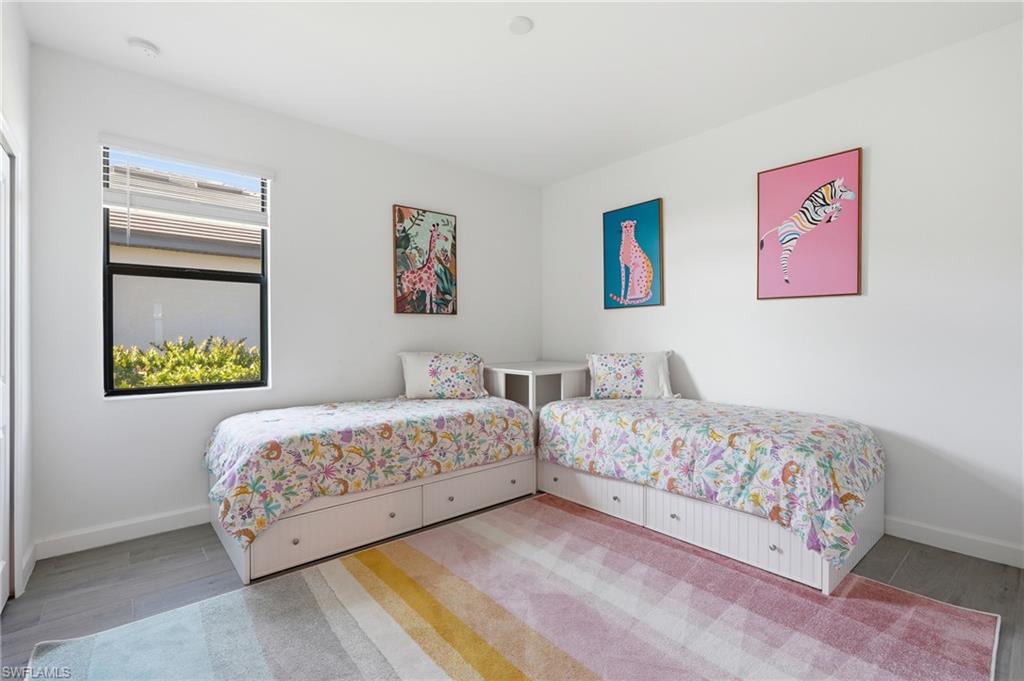 Bedroom with two single beds, floral bedding, pastel striped rug, and framed animal artwork.