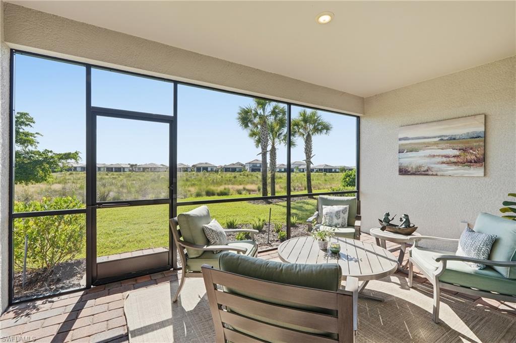 Covered patio with cushioned seating overlooks a grassy preserve and palm trees.