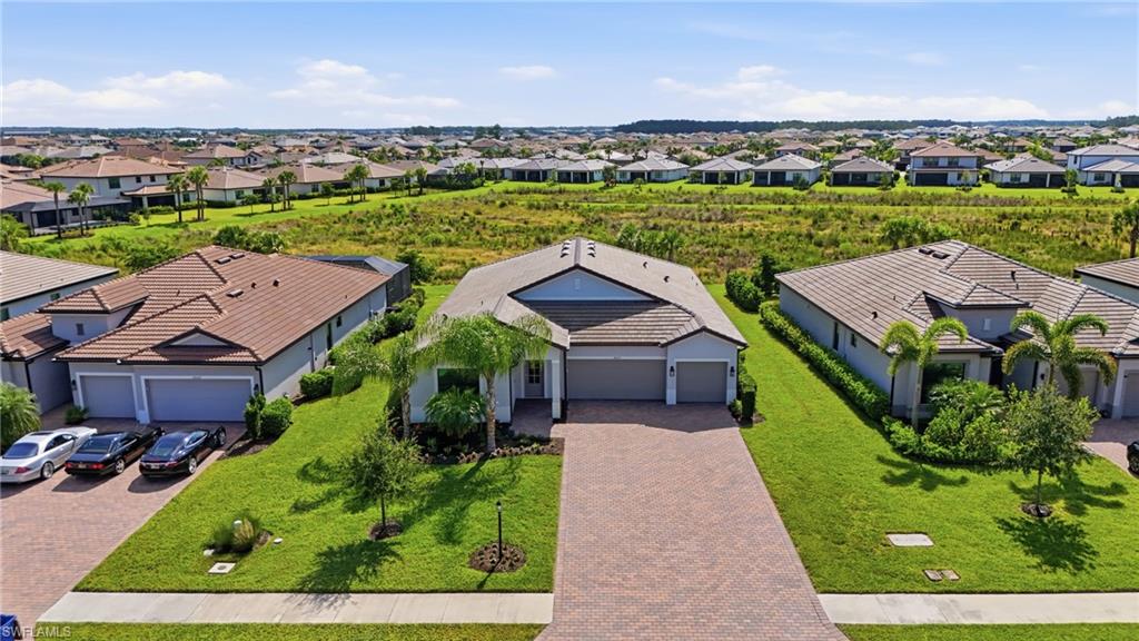 Aerial view of a single-story home with a paver driveway beside a wide greenbelt.