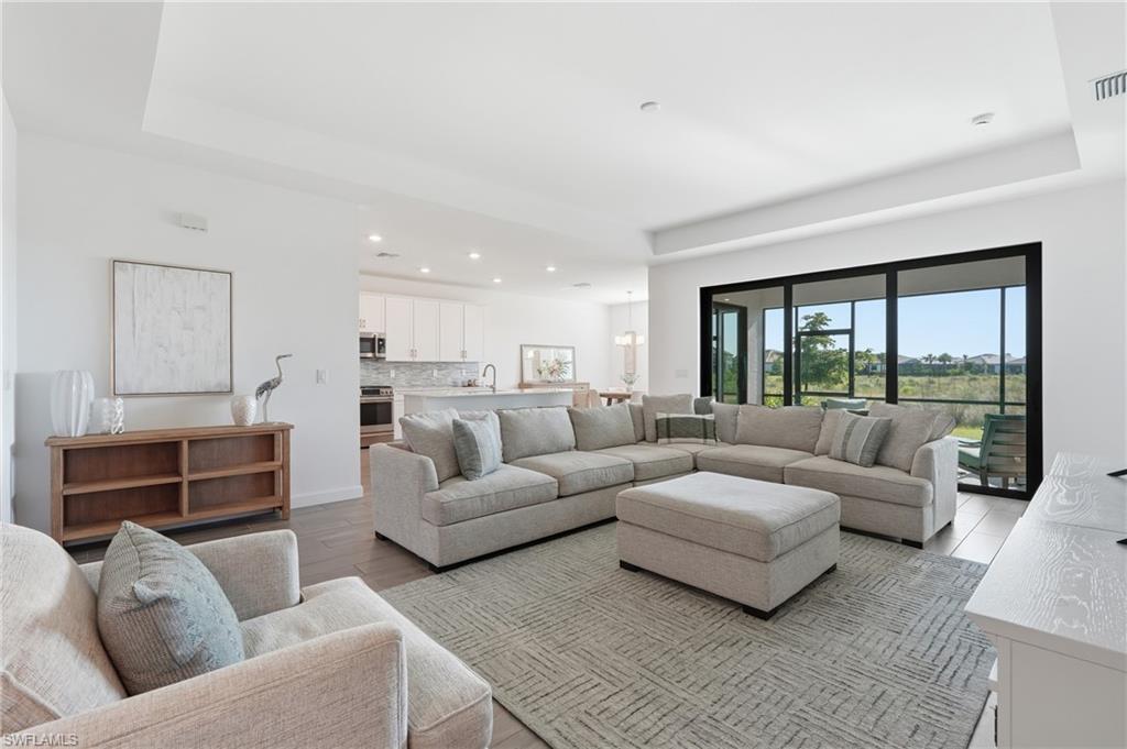 Furnished living room with a large sectional, open kitchen, and sliding glass doors overlooking the lawn.