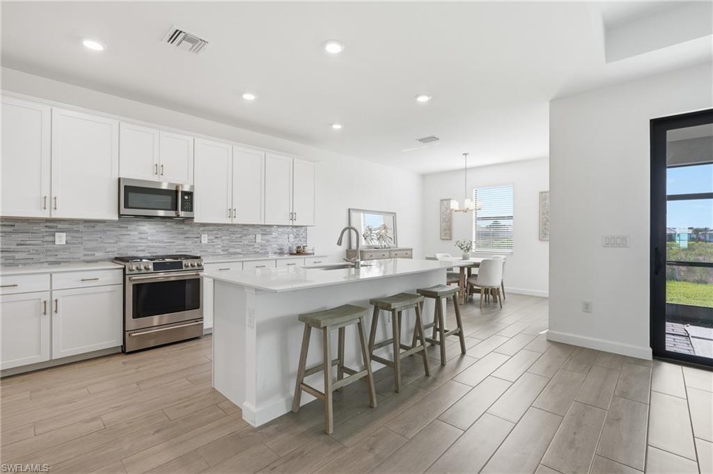 Open kitchen with a large island, four stools, white cabinets, and stainless steel appliances.