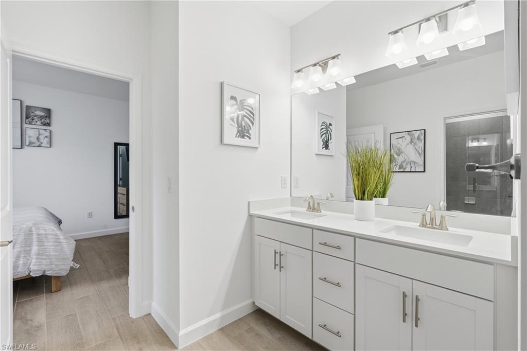 Modern bathroom with a white double-sink vanity, large mirror, and bedroom visible through the doorway.
