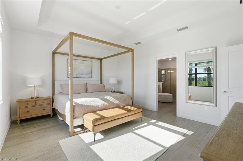 Furnished bedroom with a light wood canopy bed, cushioned bench, and sunlight across the floor.
