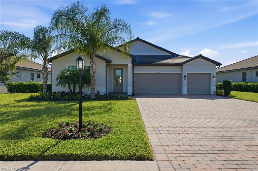 Single-story home with a two-car garage, paver driveway, and palm trees across the front lawn.
