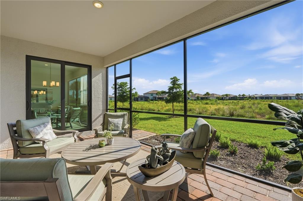 Screened lanai with cushioned seating overlooking a grassy preserve.