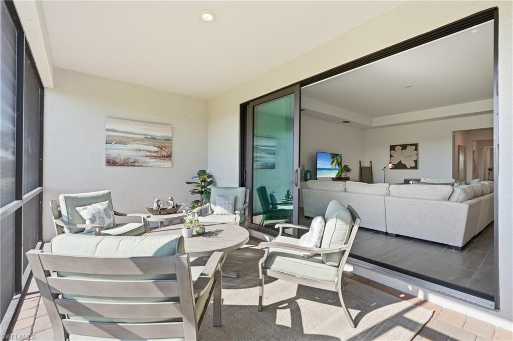 Furnished patio with cushioned seating and tables beside open sliding doors to the living room.