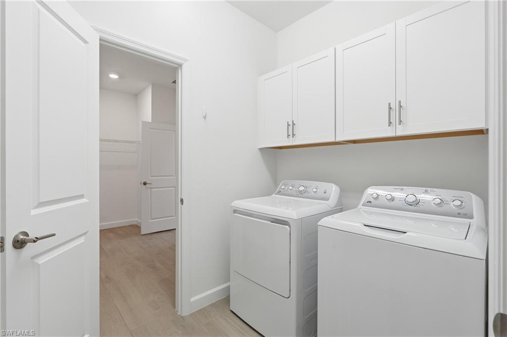 Laundry room with white washer and dryer, overhead cabinets, and light wood-look flooring.